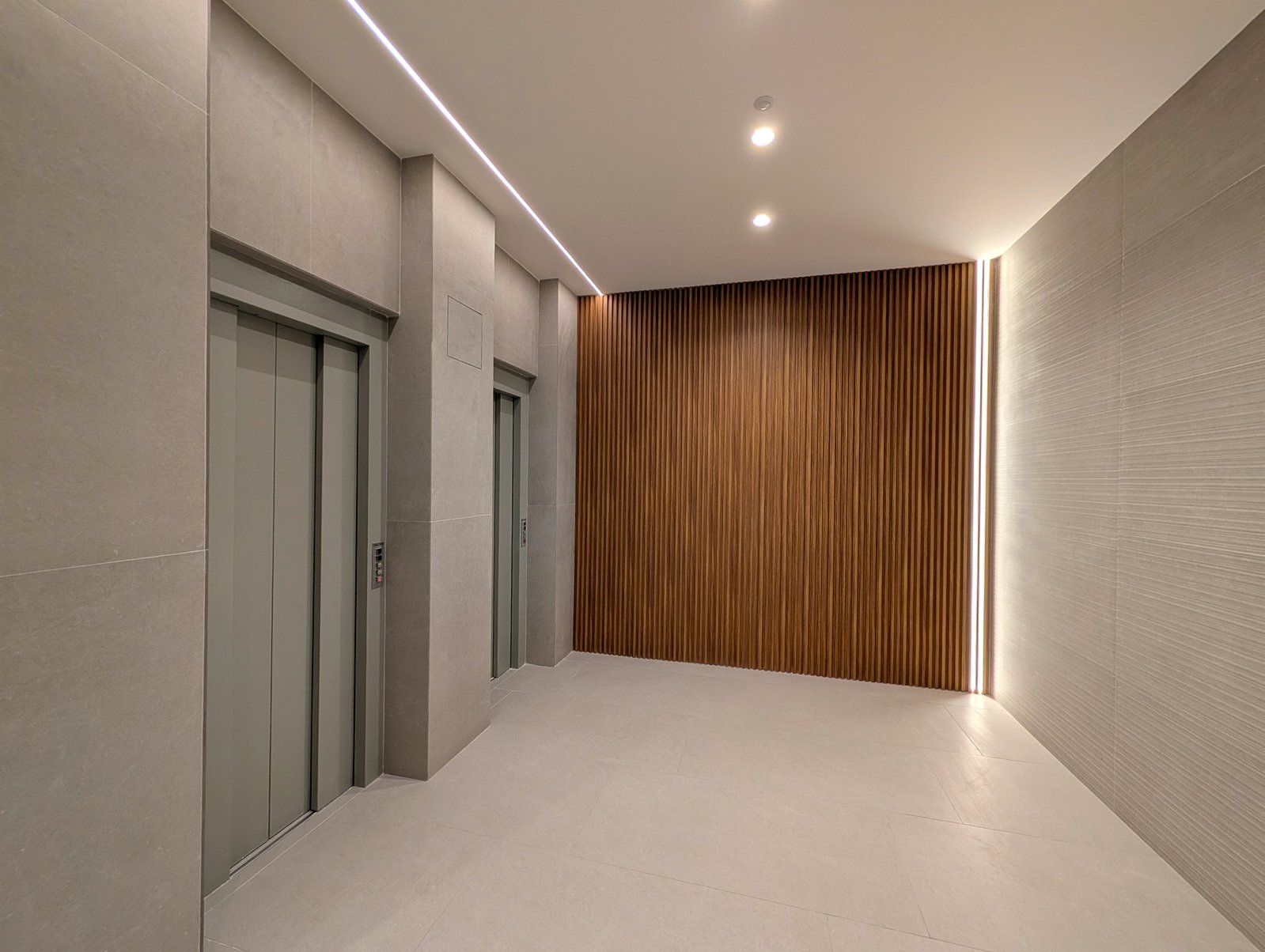 Zona de ascensores rehabilitada con listones verticales de madera e iluminación LED perimetral · Grupo Illescas