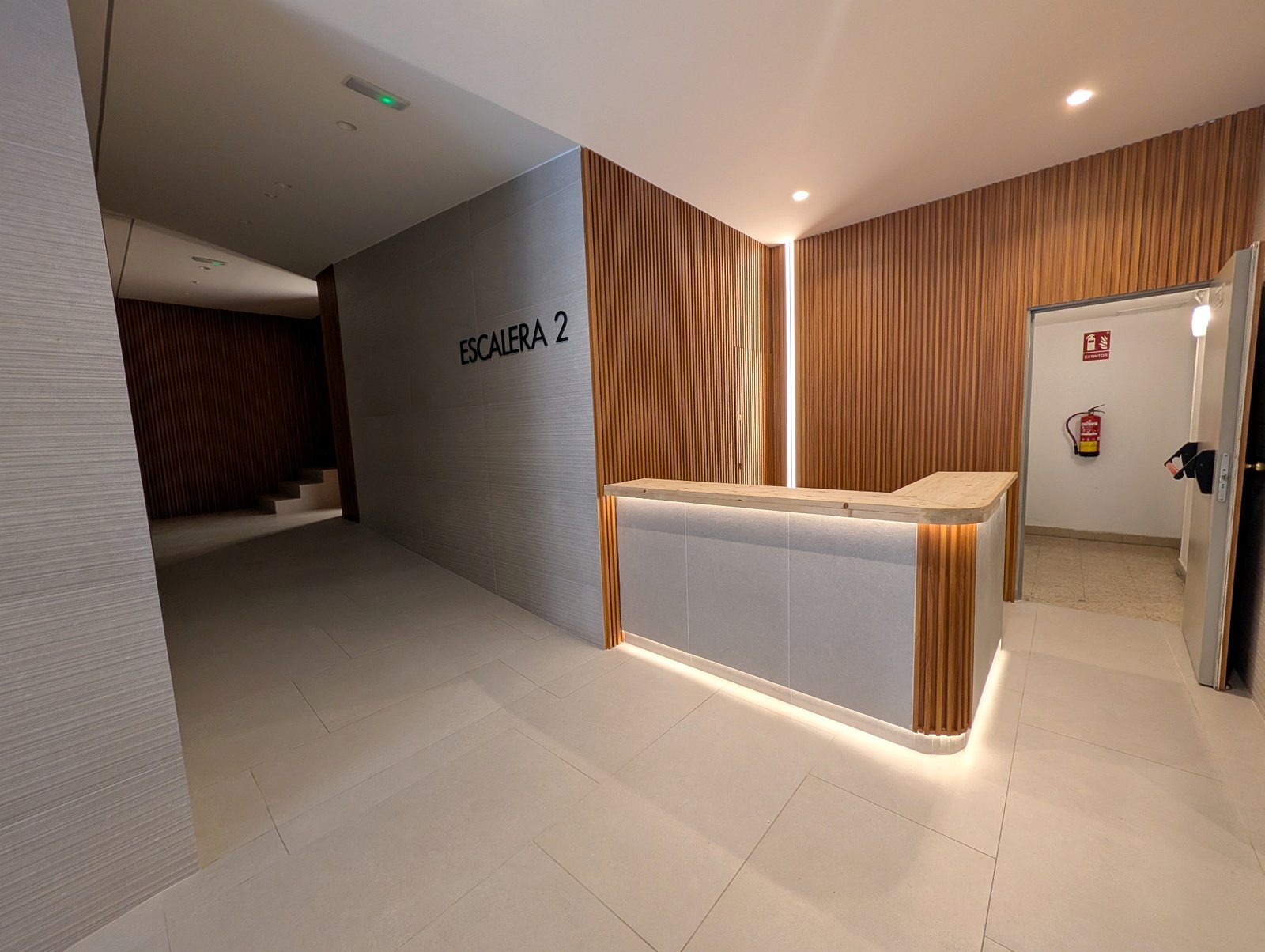 Portal rehabilitado con listones de madera, iluminación LED integrada y señalética moderna · Grupo Illescas Madrid